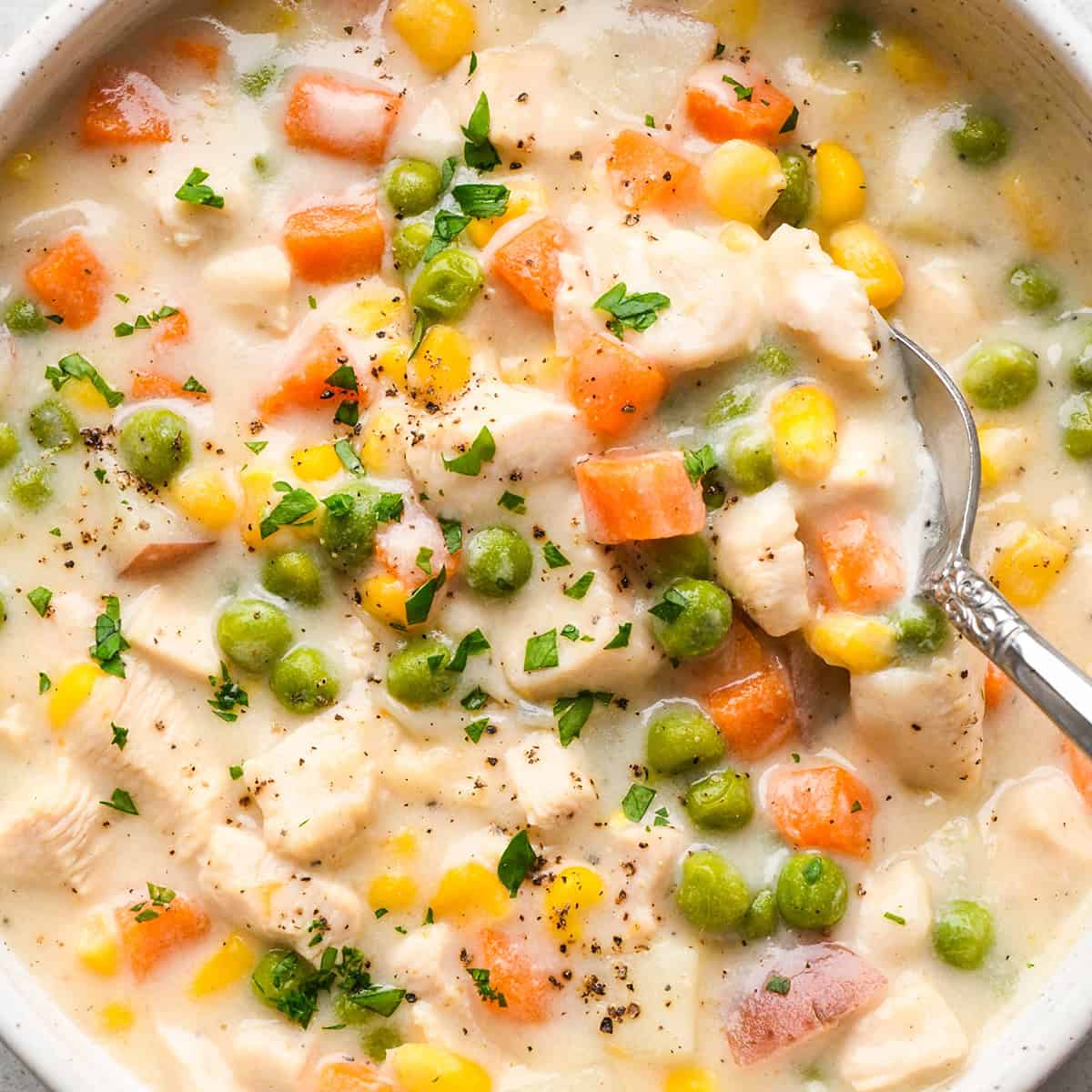 up close photo of a spoon taking a scoop of Chicken Pot Pie Soup in a bowl garnished with parsley and pepper