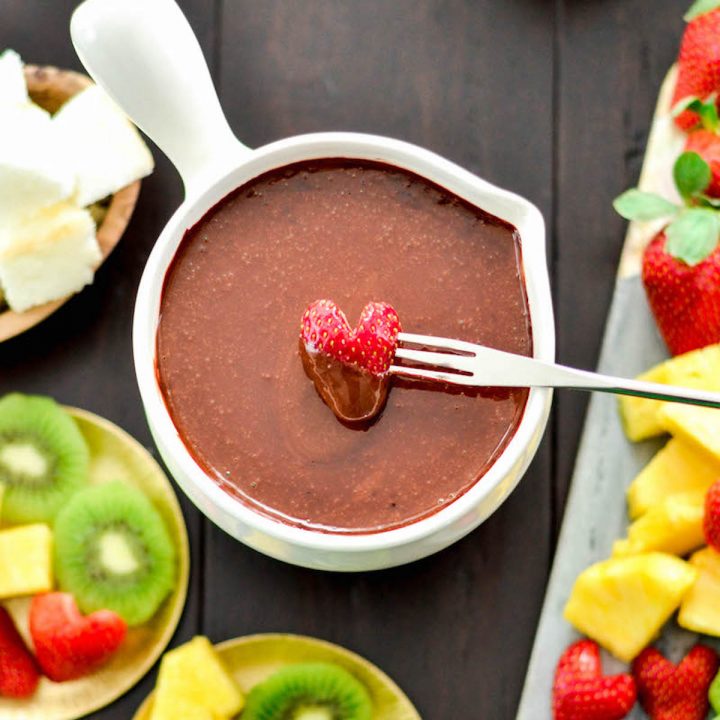 Overhead view of a heart-shaped strawberry being dipped into a bowl of Vegan Chocolate Fondue