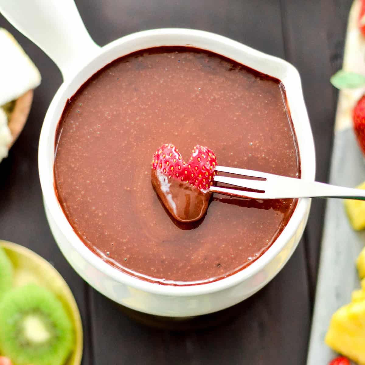 Overhead view of a heart-shaped strawberry being dipped into a bowl of Vegan Chocolate Fondue