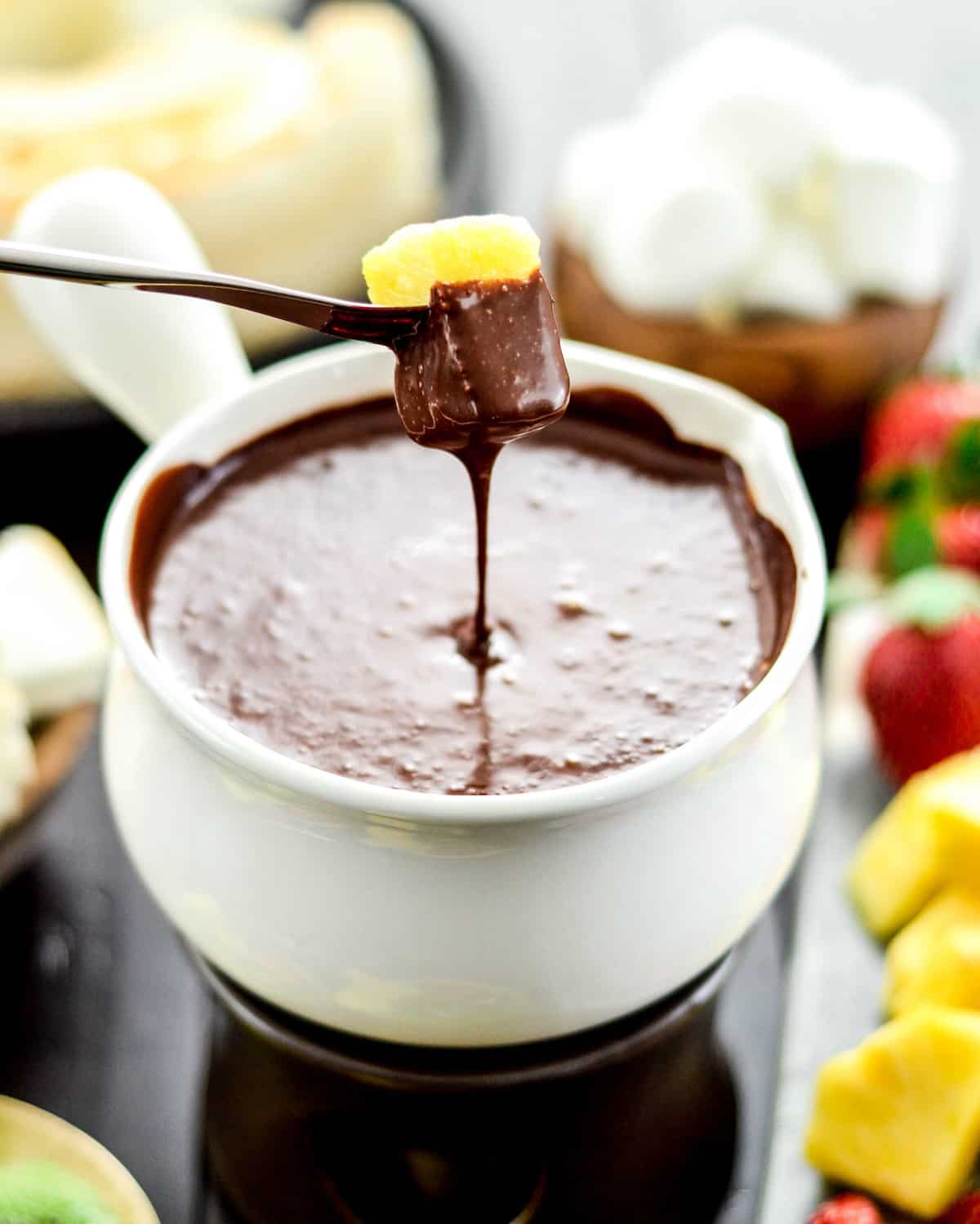 Front view of a piece of pineapple being dipped into a bowl of Vegan Chocolate Fondue