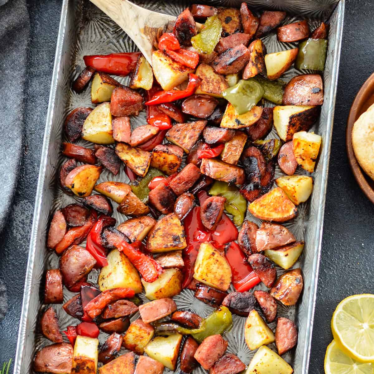 sausage and potatoes and peppers on a sheet pan with a spoon