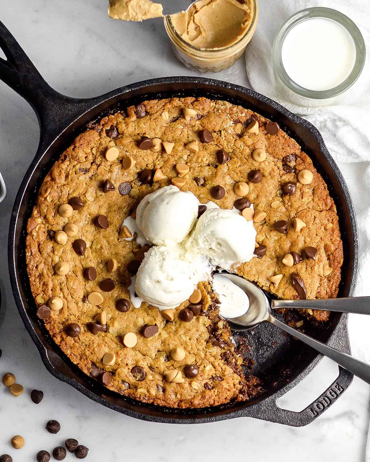 Skillet Peanut Butter Cookie with a piece cut out of it and 3 scoops of ice cream on top and two spoons