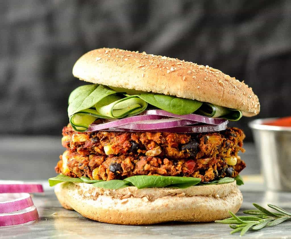 Front view of a Sweet Potato Black Bean Burgers with two patties on a bun with lettuce and red onion