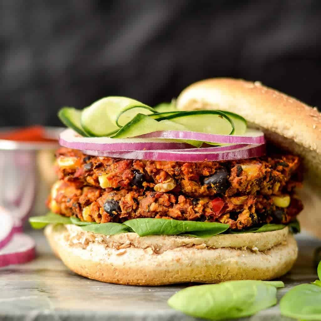 Front view of a Baked Black Bean & Sweet Potato Veggie Burger with two patties on a bun with lettuce and red onion