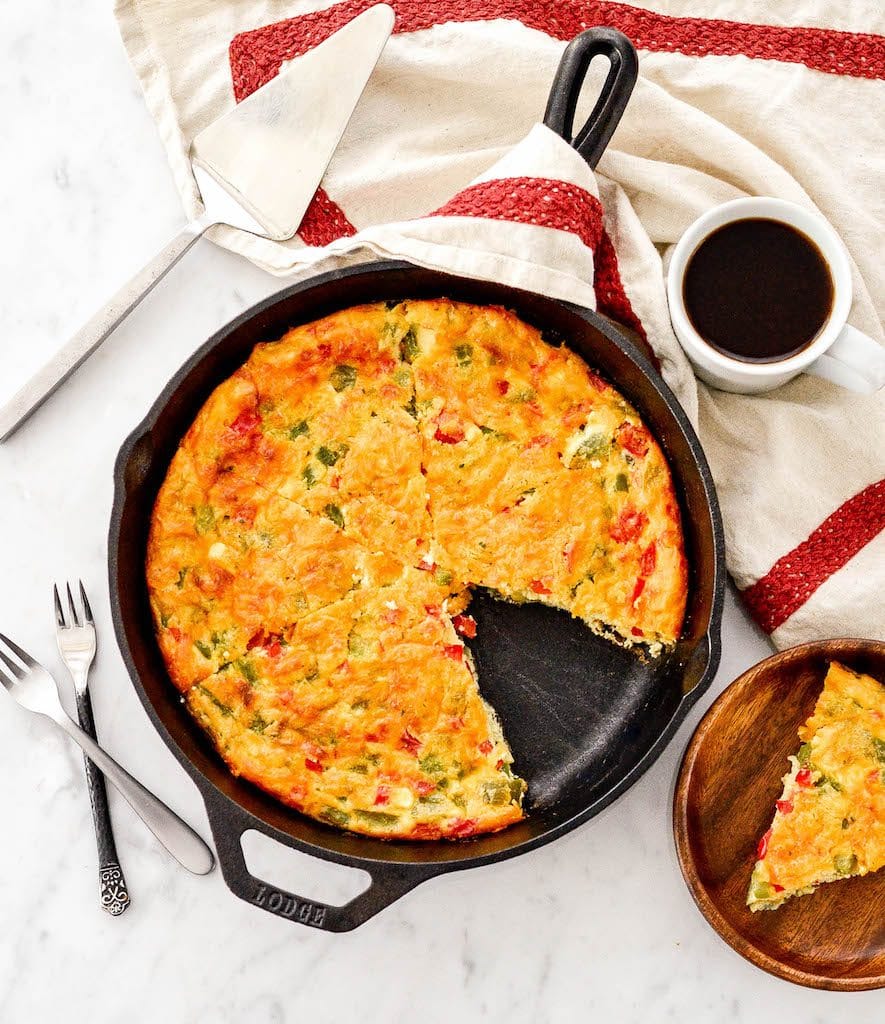 Overhead view of Gluten-Free Crustless Quiche cut into pieces with one removed on a plate next to the pan