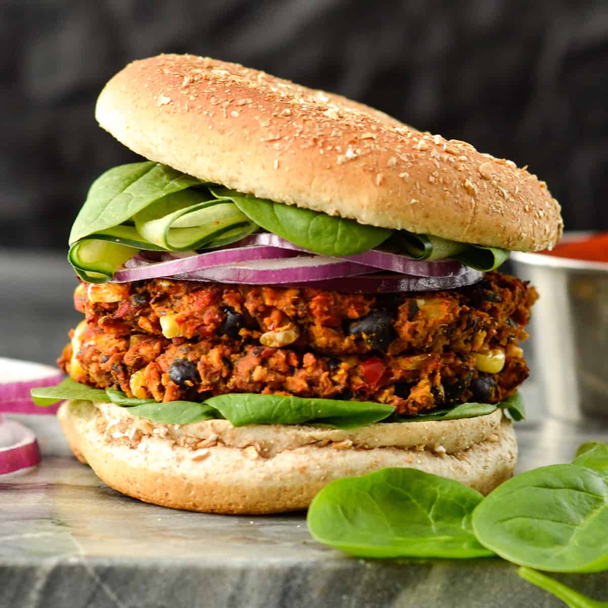 Front view of a Baked Black Bean Sweet Potato Burger with two patties on a bun with lettuce and red onion