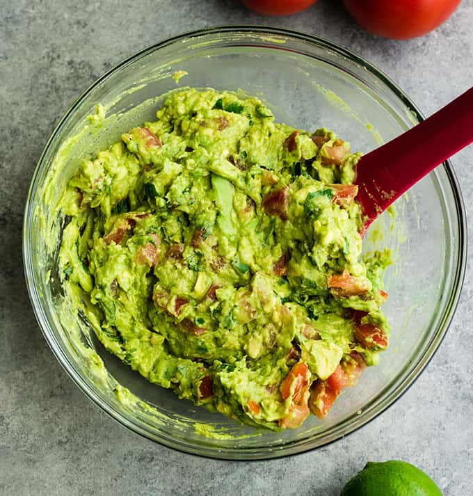 This quick & easy guacamole recipe is made with a handful of healthy ingredients and is ready in 5 minutes! This simple guacamole dip is our favorite appetizer and we always make it on taco nights! Watch the video to learn how to make this guacamole recipe! #guacamole #guacamolerecipe #tacos #appetizer #dip overhead view of a spatula stirring easy guacamole recipe in a glass bowl