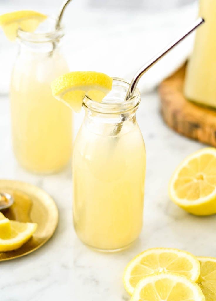 overhead view of two glass bottles filled with Healthy Lemonade with Orange Blossom water with the pitcher of healthy lemonade in the background