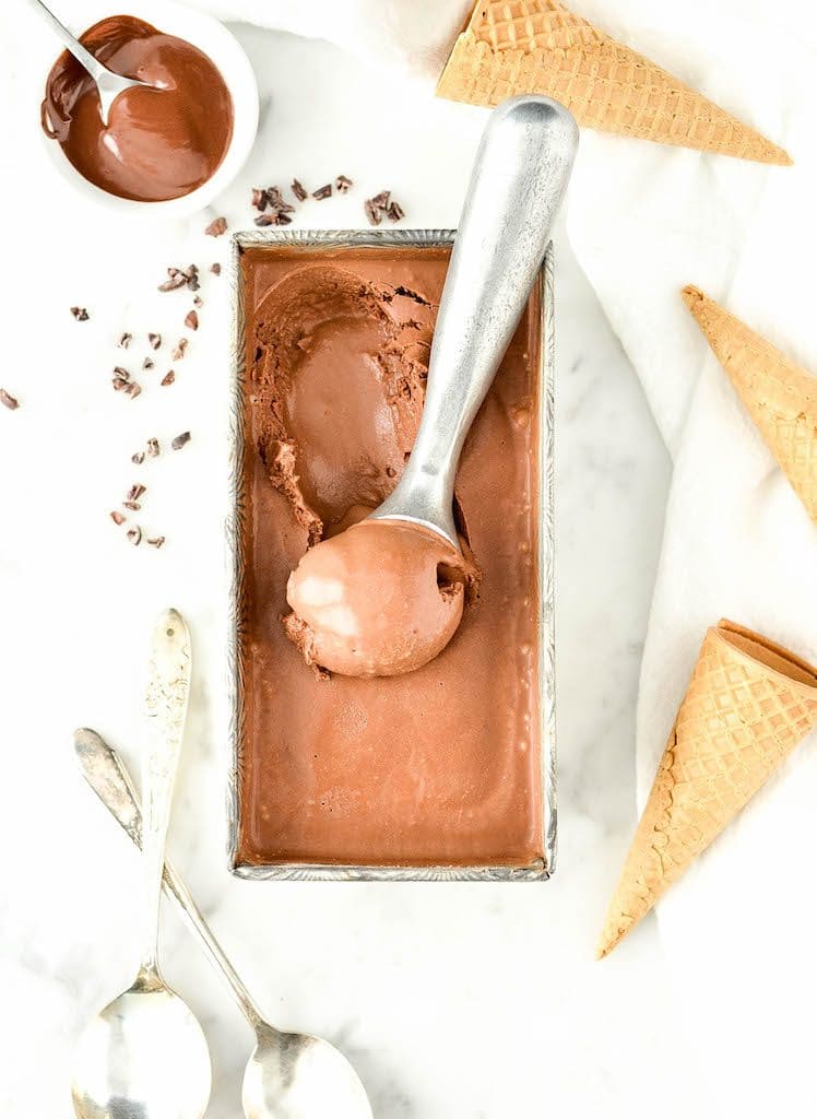 overhead view of a rectangular container of paleo chocolate ice cream with an ice cream scoop scooping out a scoop of it