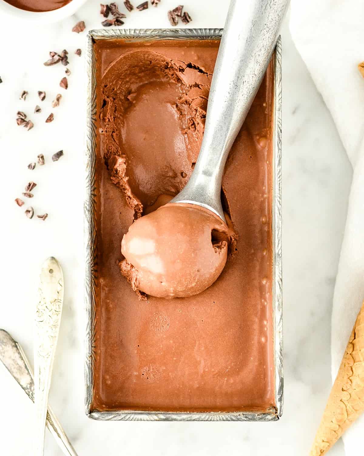 an ice cream scoop taking a scoop of Paleo Chocolate Ice Cream out of a container
