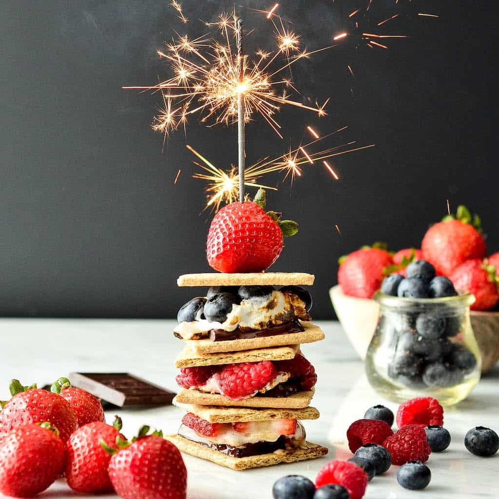 Front view of a stack of three Dark Chocolate S'mores with Fresh Berries with a sparkler on top