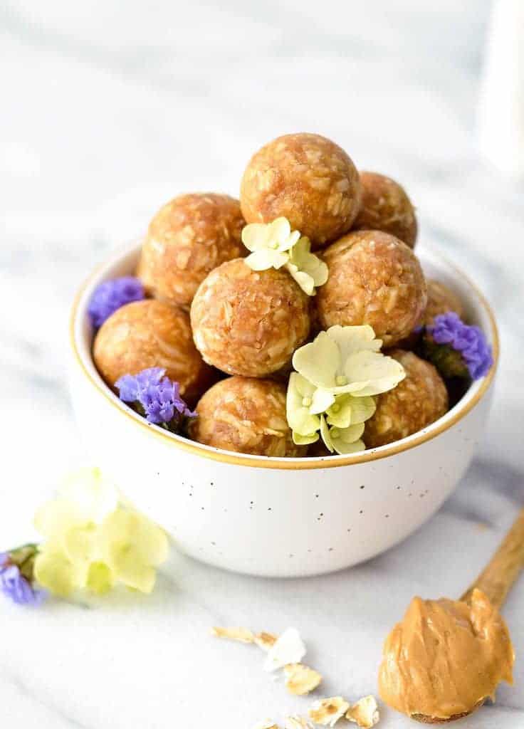 Side & overhead view of Peanut Butter Oatmeal Balls arranged in a "tower" in a white & gold bowl with flowers