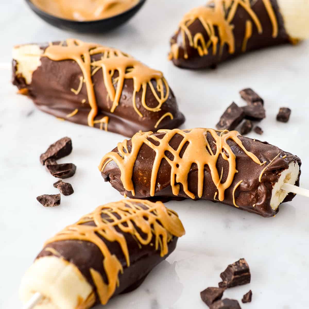 Front view of four chocolate covered frozen bananas with a peanut butter drizzle