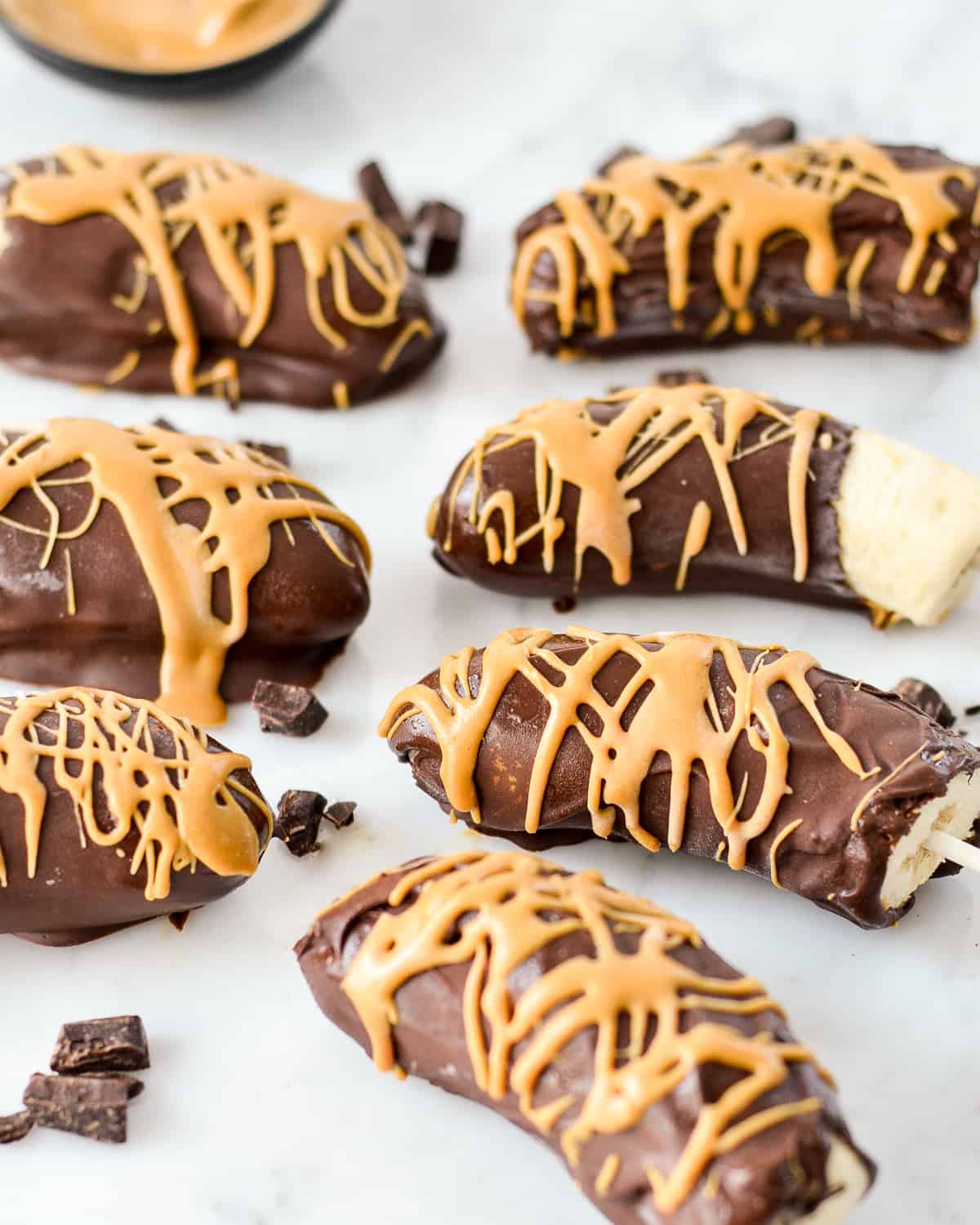 Side view of two rows of Chocolate Covered Frozen Bananas drizzled with peanut butter