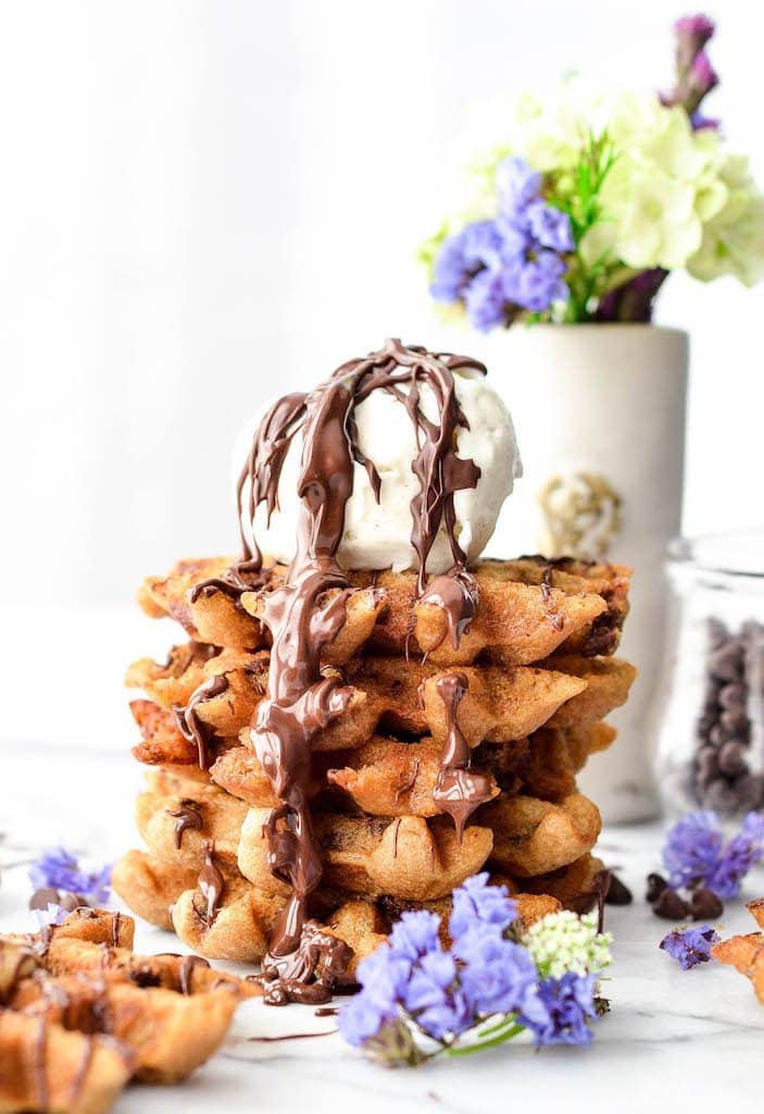 front view of a stack of five peanut butter waffles with a scoop of vanilla ice cream and a drizzle of chocolate on top