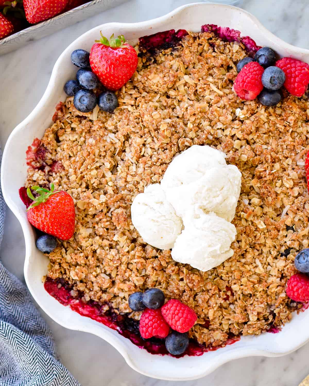 Overhead view of Healthy Berry Crisp Recipe garnished with fresh berries and vanilla ice cream