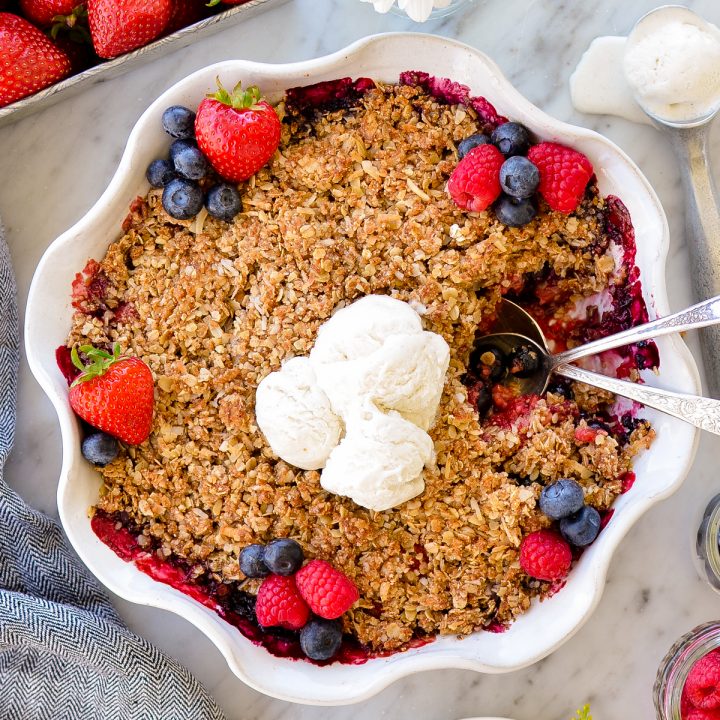 Overhead view of Healthy Berry Crisp Recipe in a pie dish with a plate of Healthy Berry Crisp Recipe on the side and two spoons in the dish