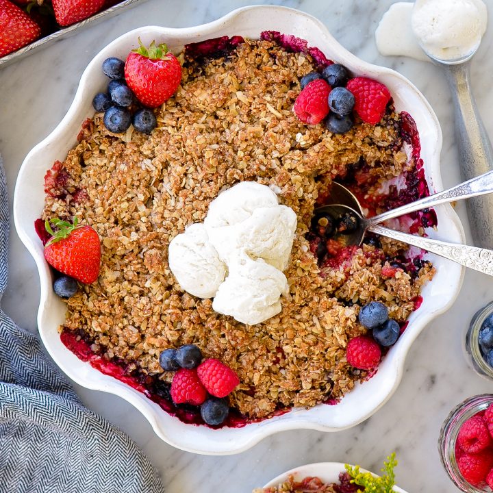 Overhead view of Healthy Berry Crisp Recipe in a pie dish garnished with fresh berries and vanilla ice cream