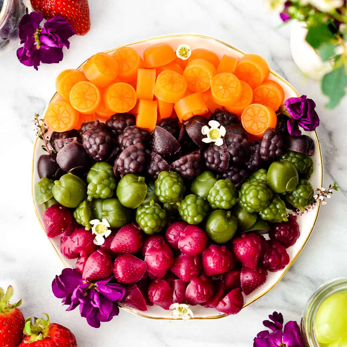 Overhead view of a plate of Homemade Fruit Snacks arranged by color (orange on top, then purple then green then magenta). 