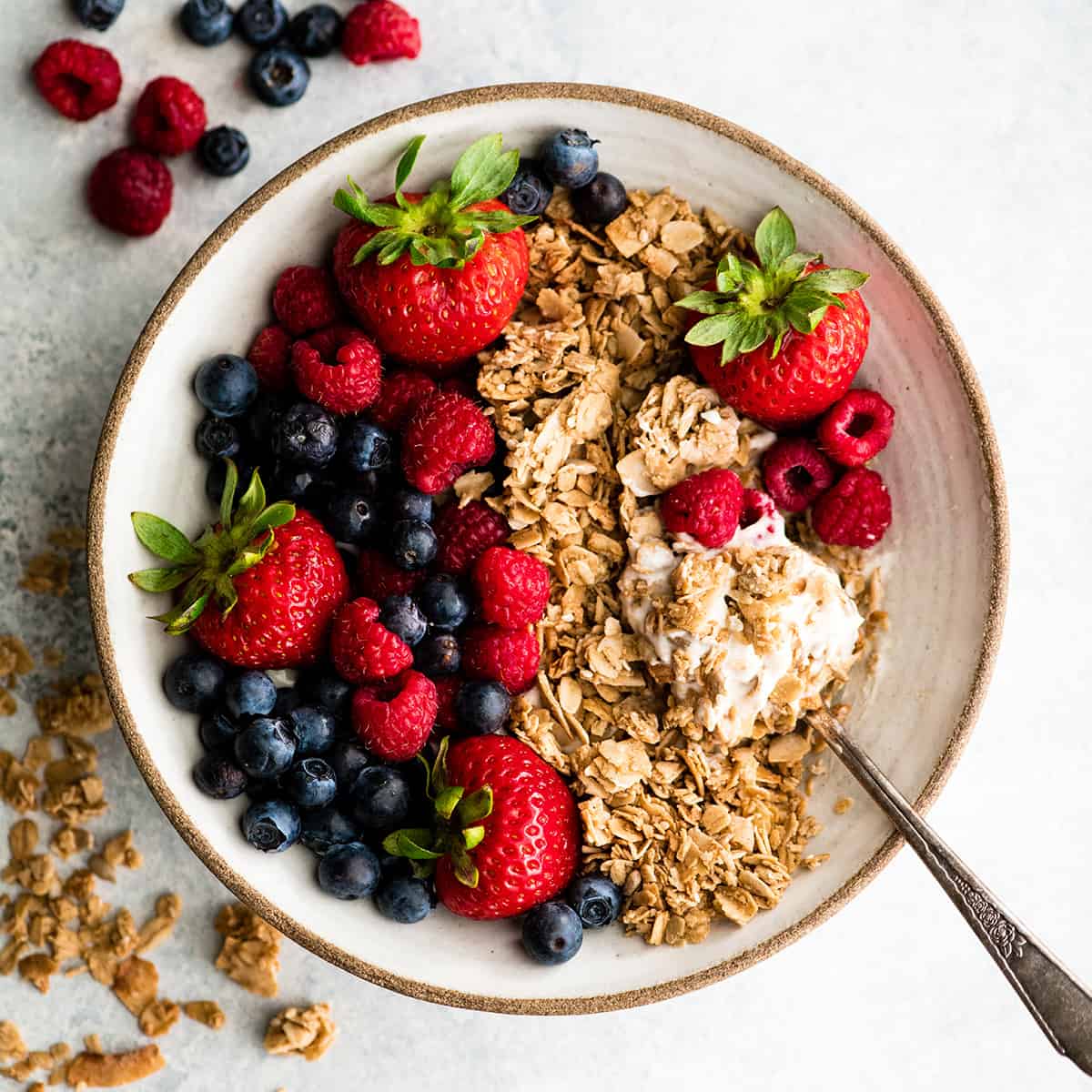 a bowl of healthy homemade granola over yogurt with berries and a spoon taking a bite out of it