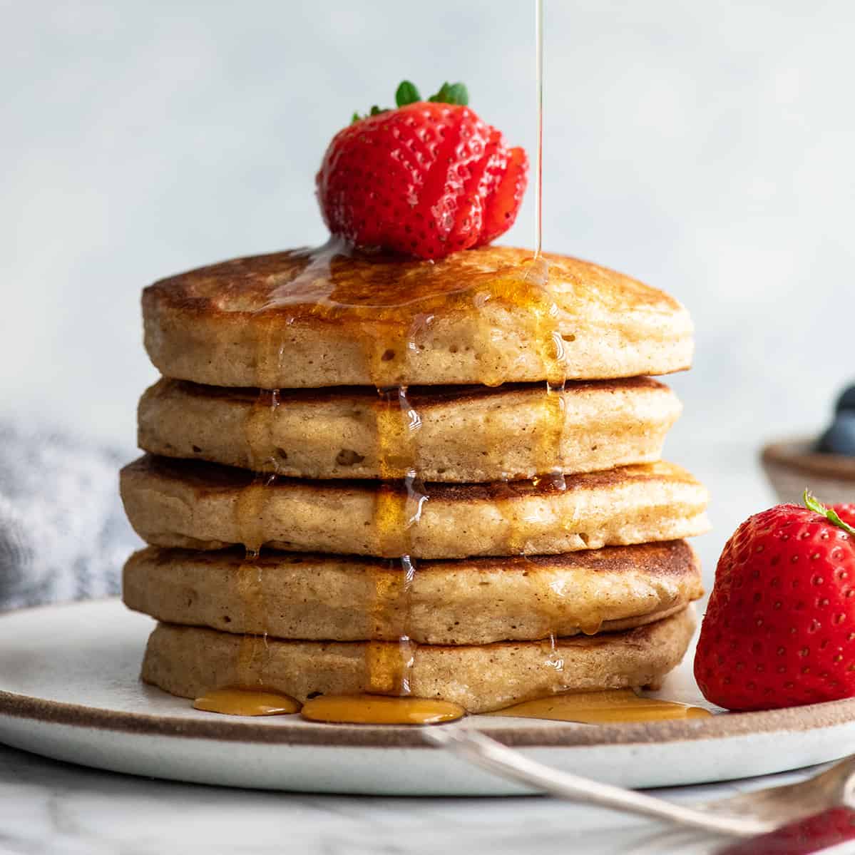 front view of a stack of 5 whole wheat pancakes with syrup pouring on them
