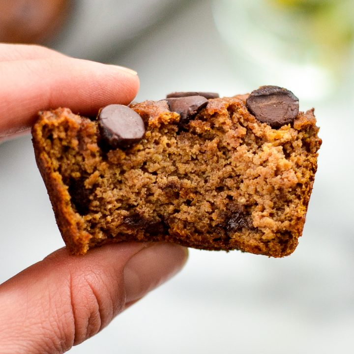 Front view of a hand holding a Paleo Pumpkin Muffin with a bite taken out of it