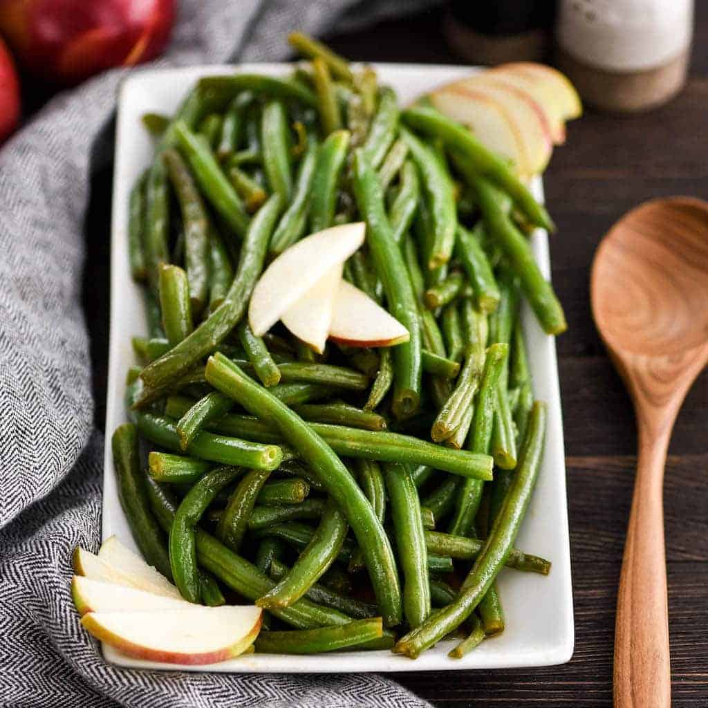Front view of Sautéed Green Beans with Apple Cider on a serving dish garnished with apple slices