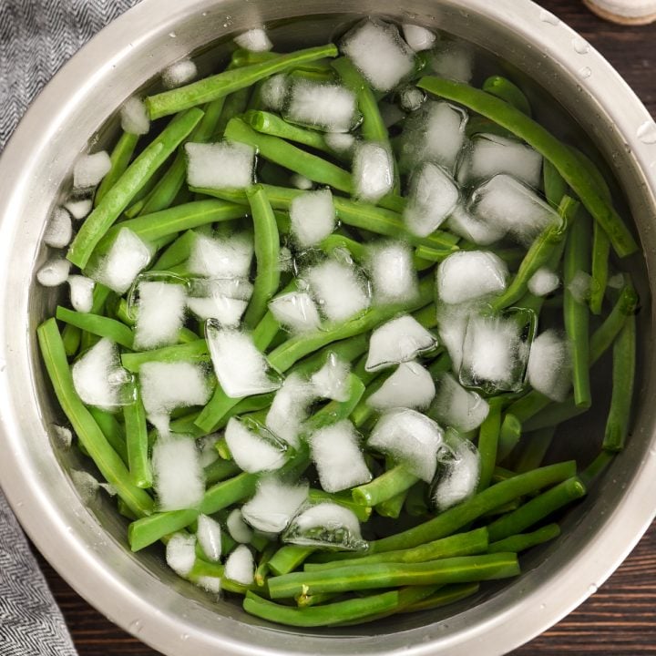Overhead view of a bowl of fresh green beans in ice water to show how to cook fresh green beans by blanching 