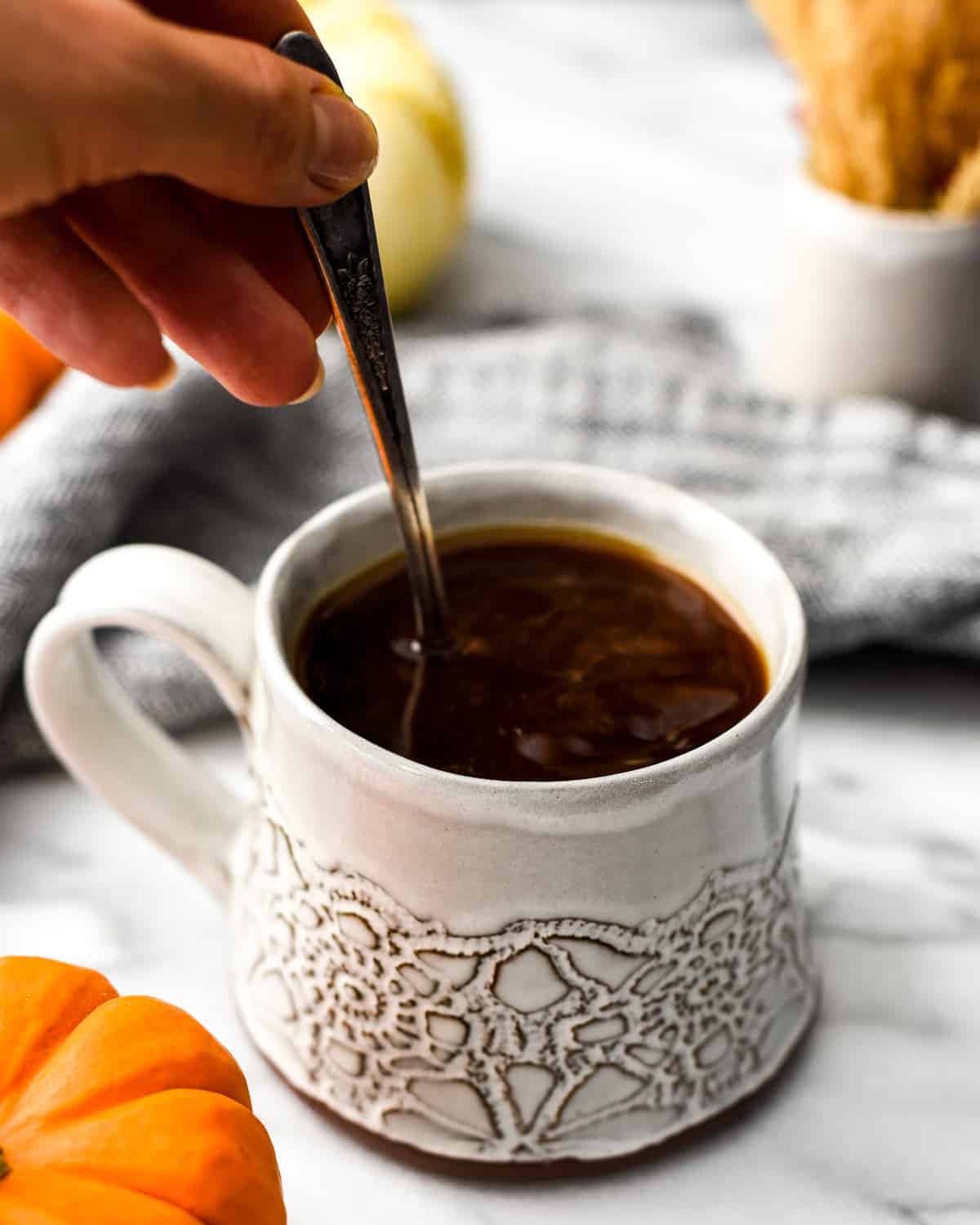Hand holding a spoon stirring Homemade Pumpkin Coffee Creamer into a cup of coffee