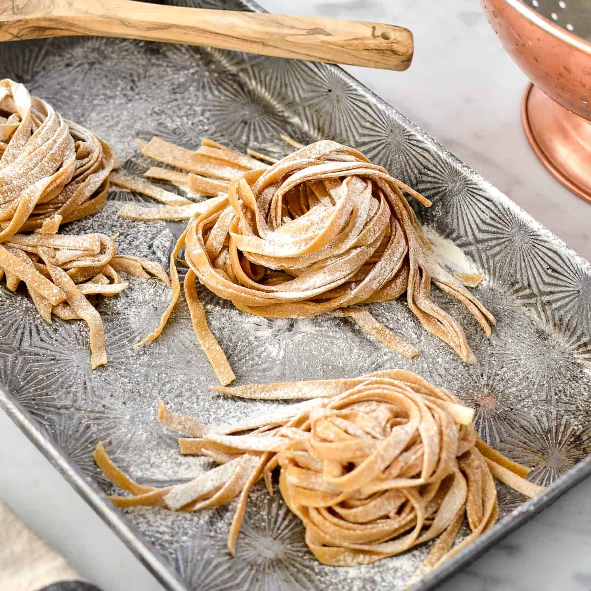 homemade whole wheat pasta before cooking covered in flour on a baking sheet