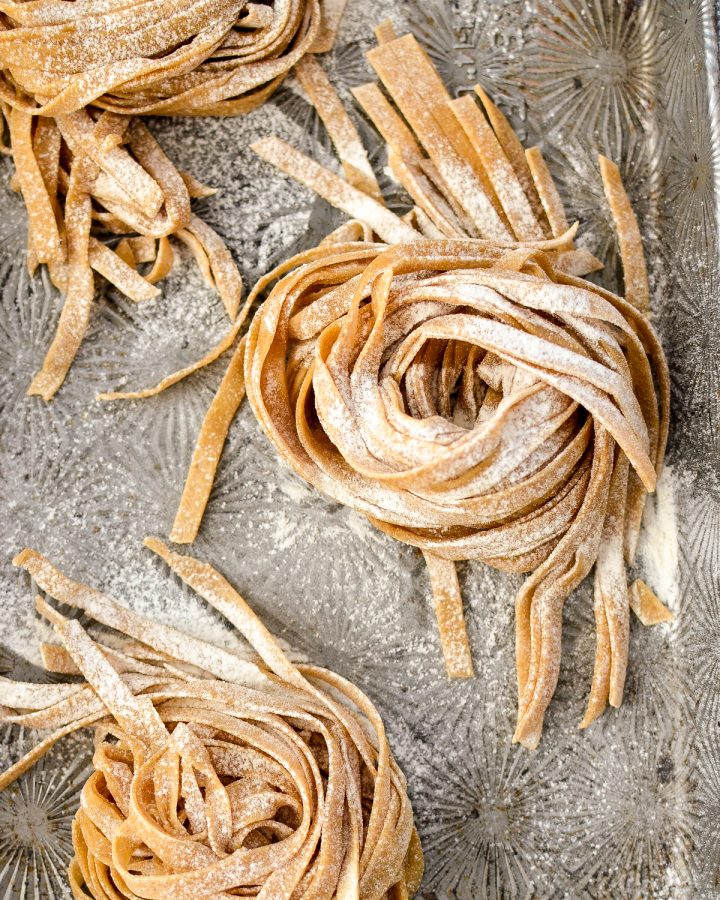 homemade whole wheat pasta before cooking covered in flour on a baking sheet