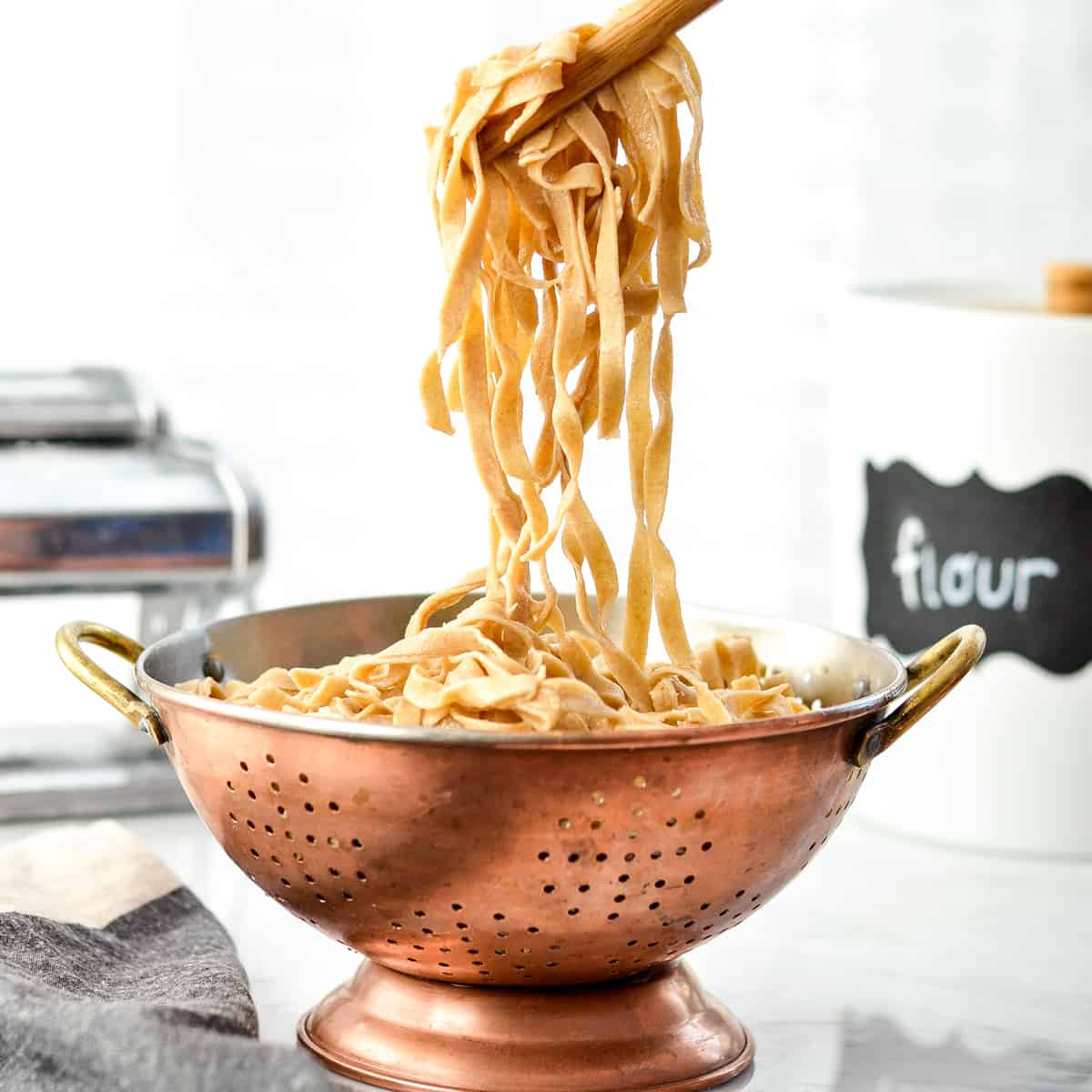Front view of cooked Homemade Whole Wheat Pasta being pulled out of a colander with wooden tongs