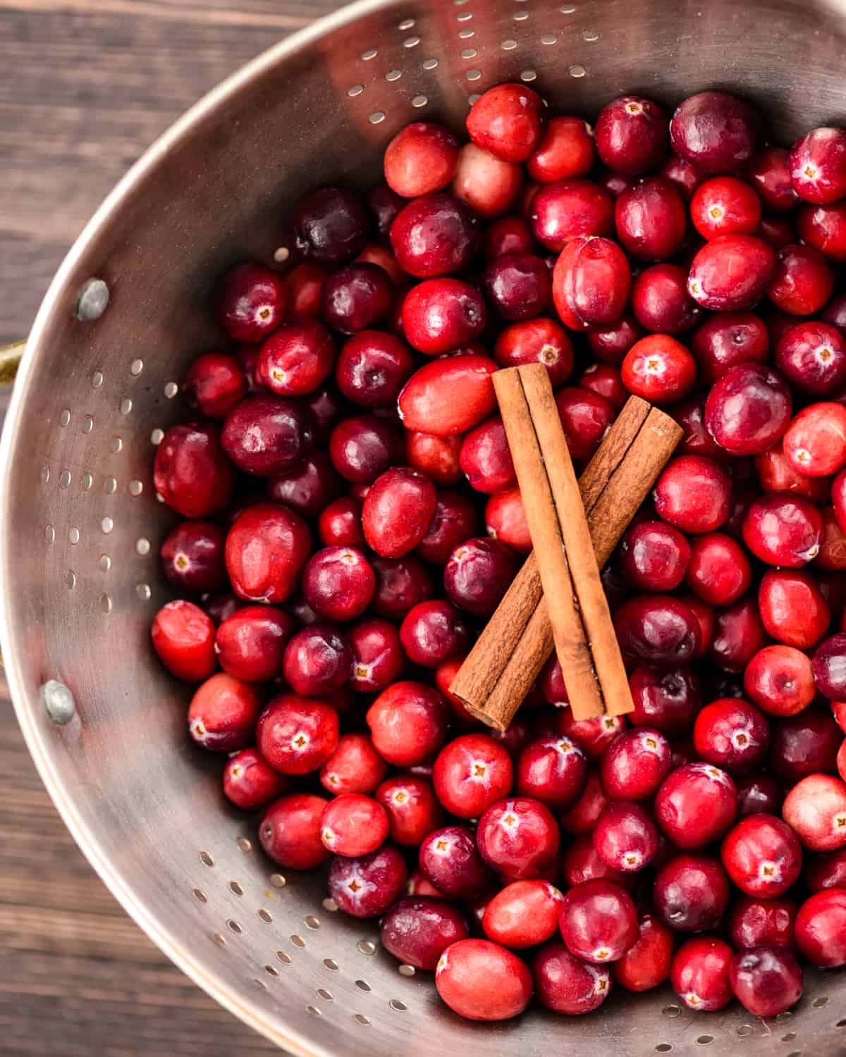 Overhead view of a colander with fresh cranberries and cinnamon sticks in it in the making of Healthy Cranberry Sauce
