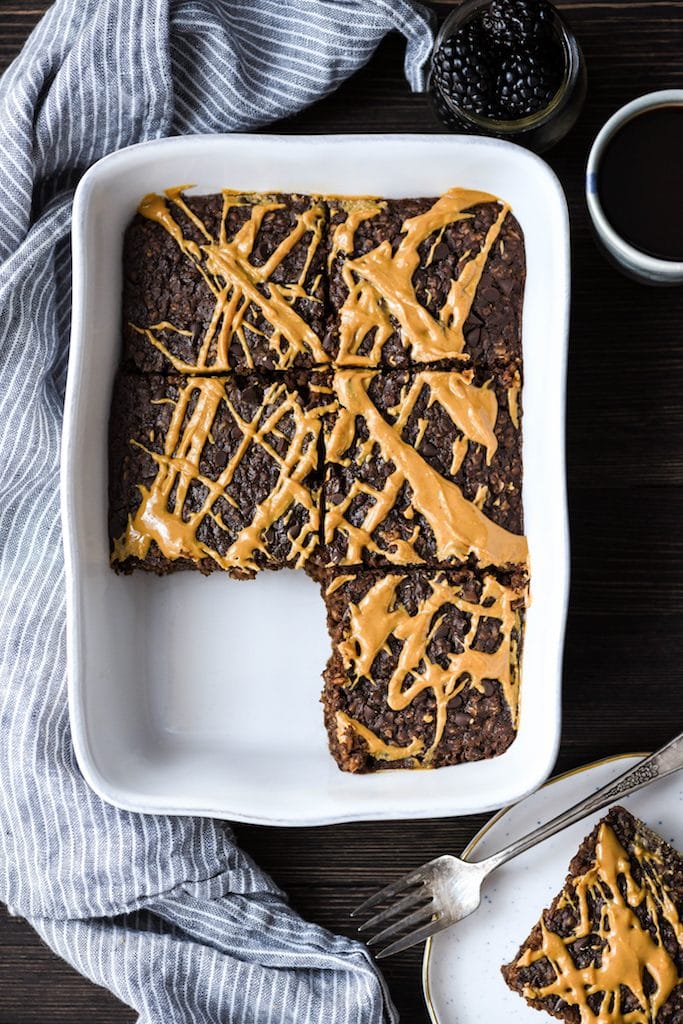 Overhead view of Healthy Chocolate Peanut Butter Baked Oatmeal cut into 6 squares with one removed on a plate next to the baking dish