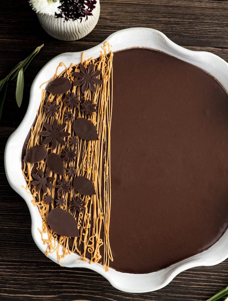 Overhead view of Chocolate Peanut Butter Pie recipe in circular pie dish with peanut butter drizzle and chocolate leaf decorations