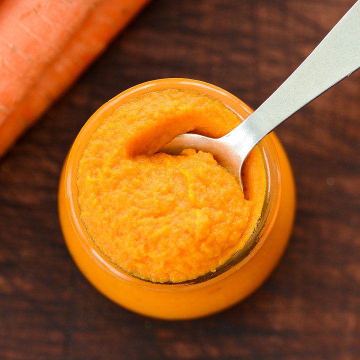 Overhead view of a glass jar of Homemade Baby Food Carrots with a baby spoon in it taking a scoop