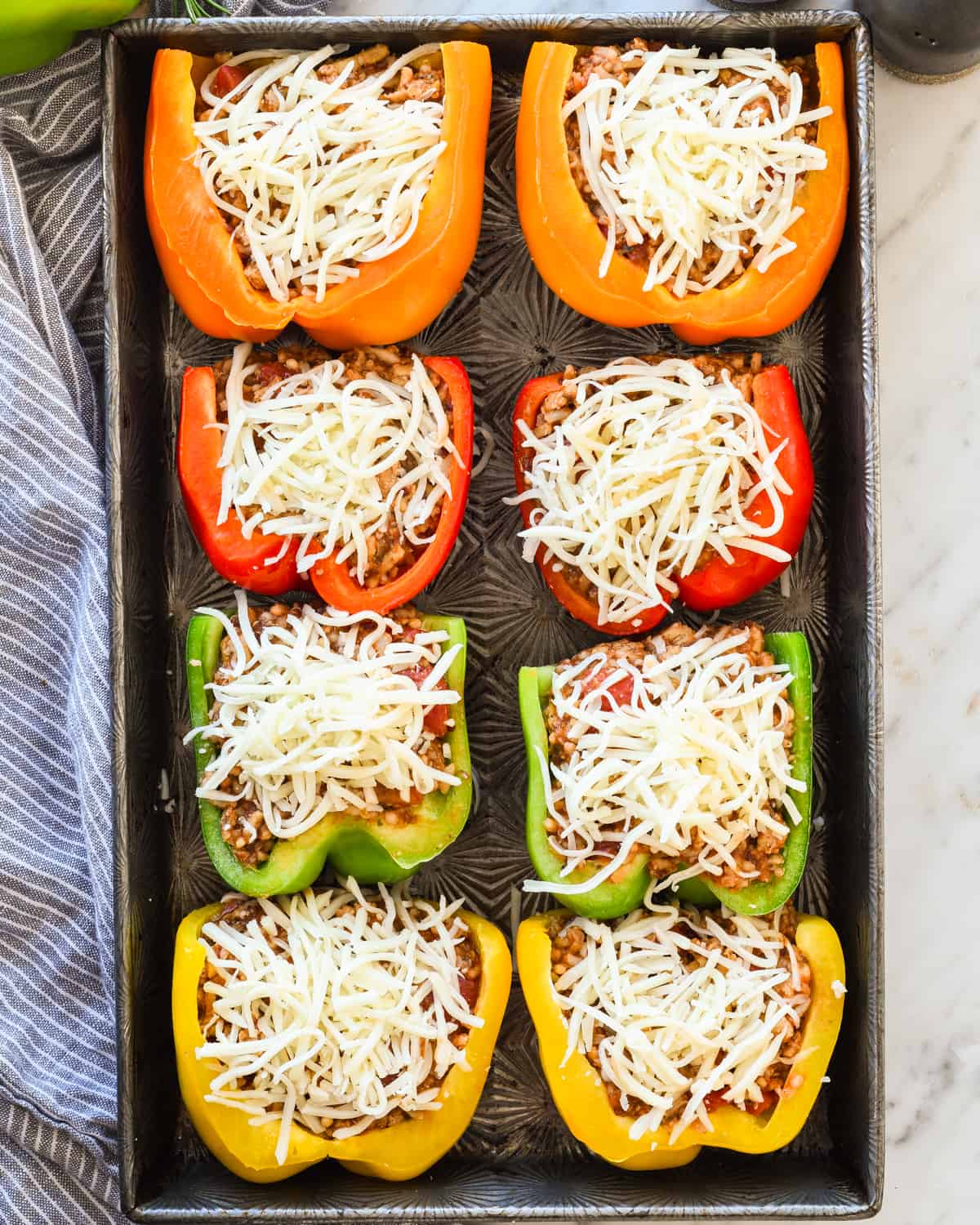 Overhead view of healthy Italian Stuffed Peppers arranged on a baking sheet with cheese sprinkled on top before baking