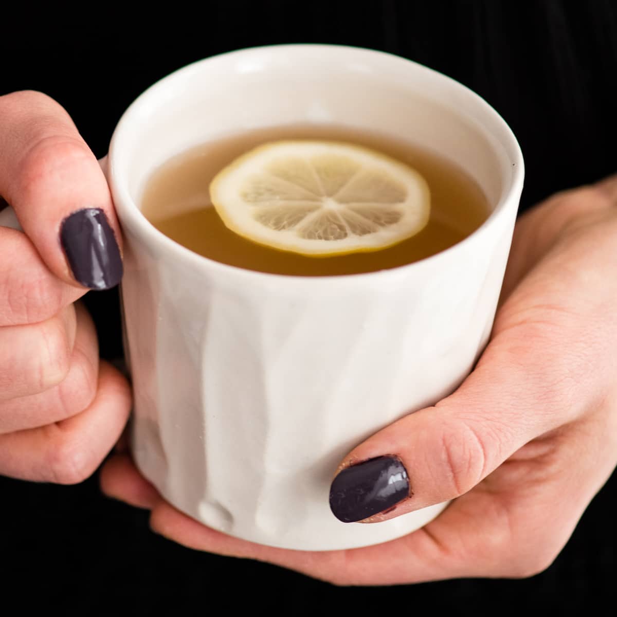 Front view of two hands holding a mug of Immune Boosting Tea Recipe with a lemon slice in it 