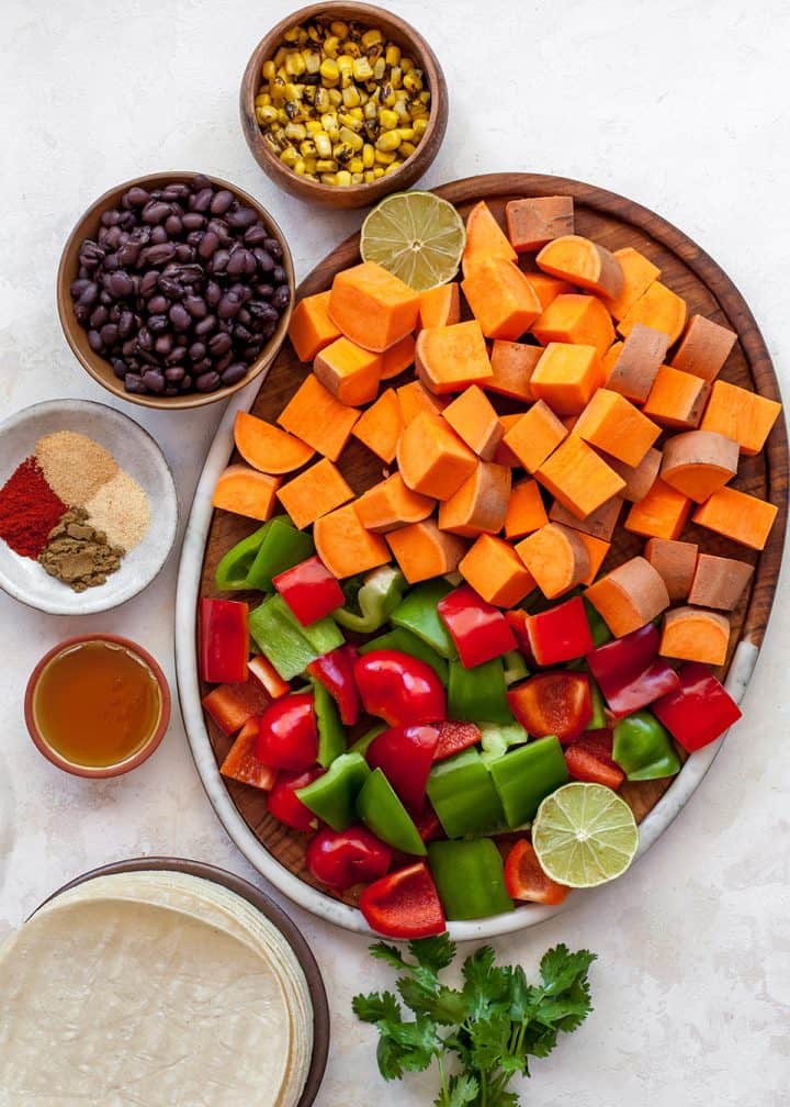 These healthy black bean sweet potato tacos are the best vegetarian tacos ever. Sweet potatoes and vegetables are perfectly spiced and roasted, then tossed with a honey, lime cilantro mixture for the most flavorful and delicious tacos. Taco night isn't complete without this sweet potato taco recipe! overhead view of the ingredients in this sweet potato tacos recipe