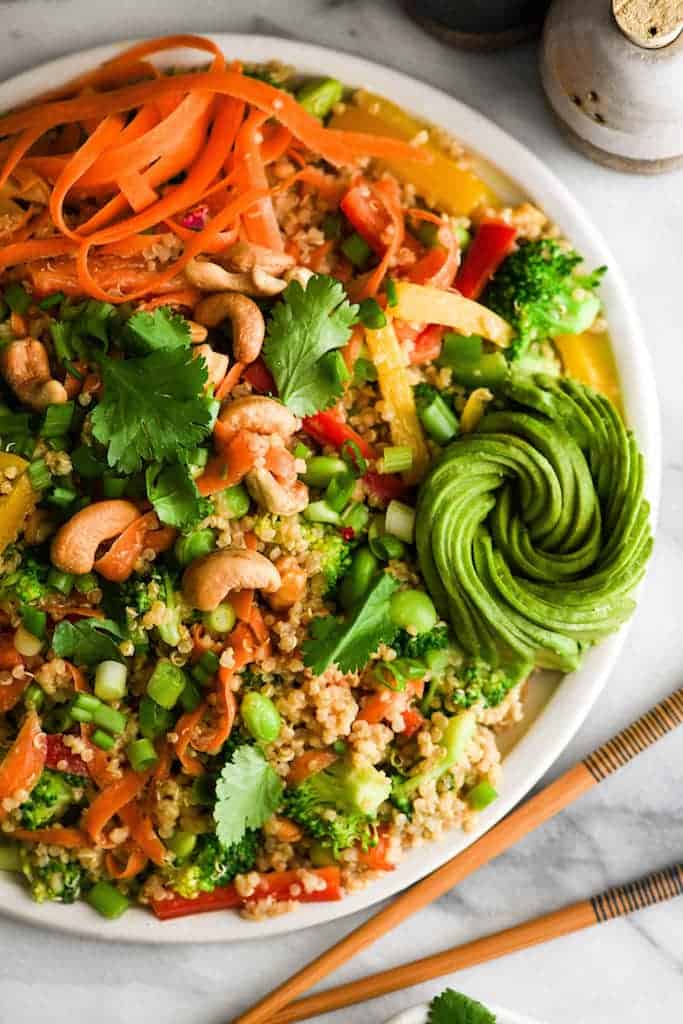  Vue aérienne d'une salade de quinoa asiatique avec vinaigrette aux arachides sur un plateau blanc rond avec une magnifique rose d'avocat 