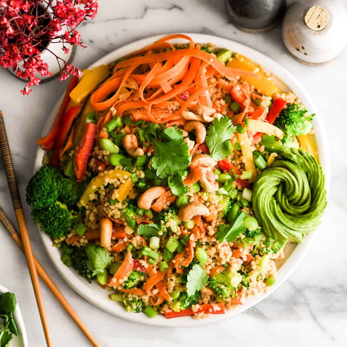 Overhead view of asian quinoa salad with peanut dressing on a round white platter with a gorgeous avocado rose 