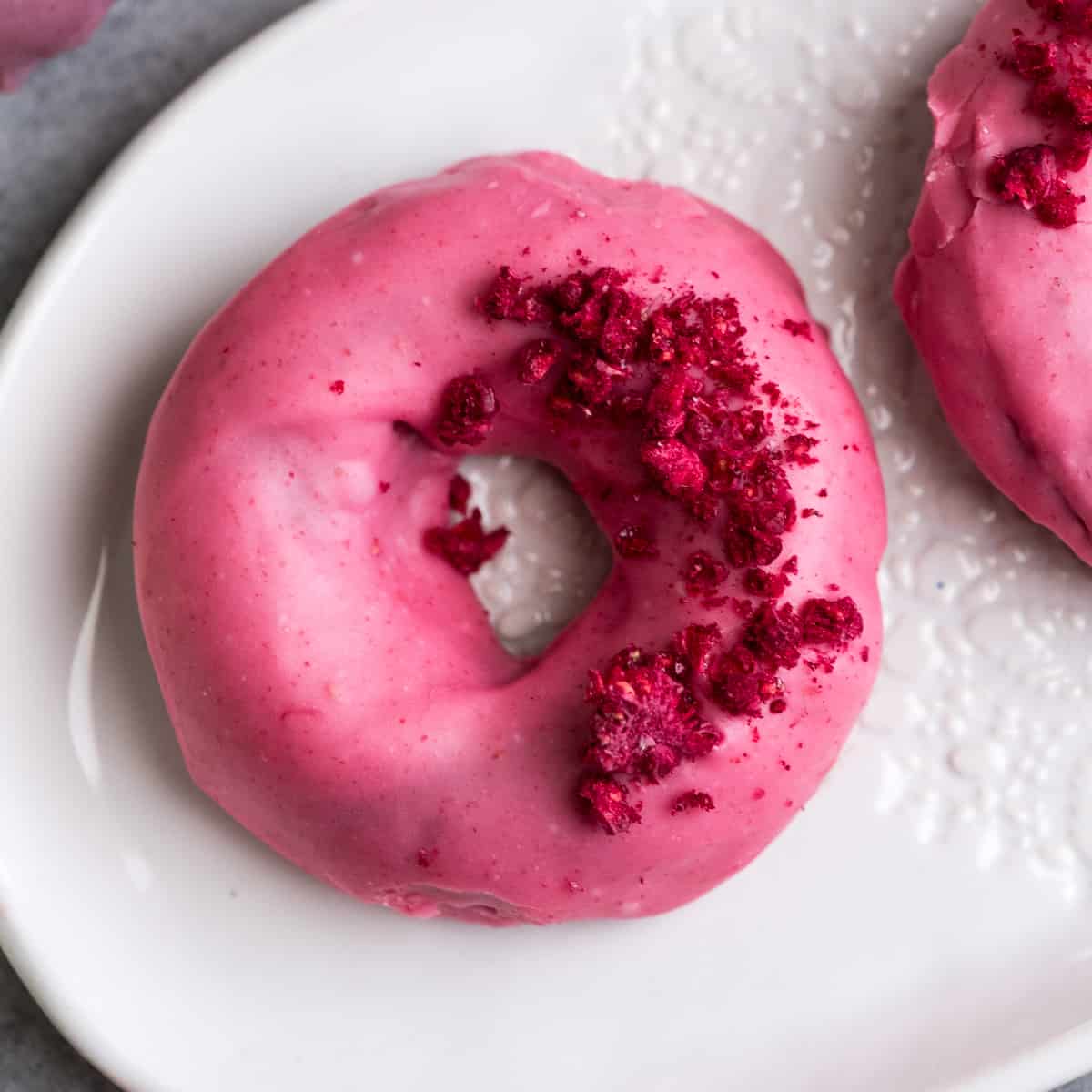Overhead view of five raspberry baked donuts with pink raspberry glazed sprinkled with dried raspberries 