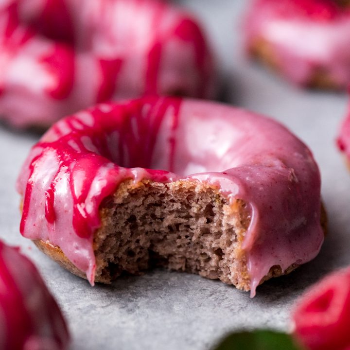 Front view of a raspberry donut with a bite taken out of it 