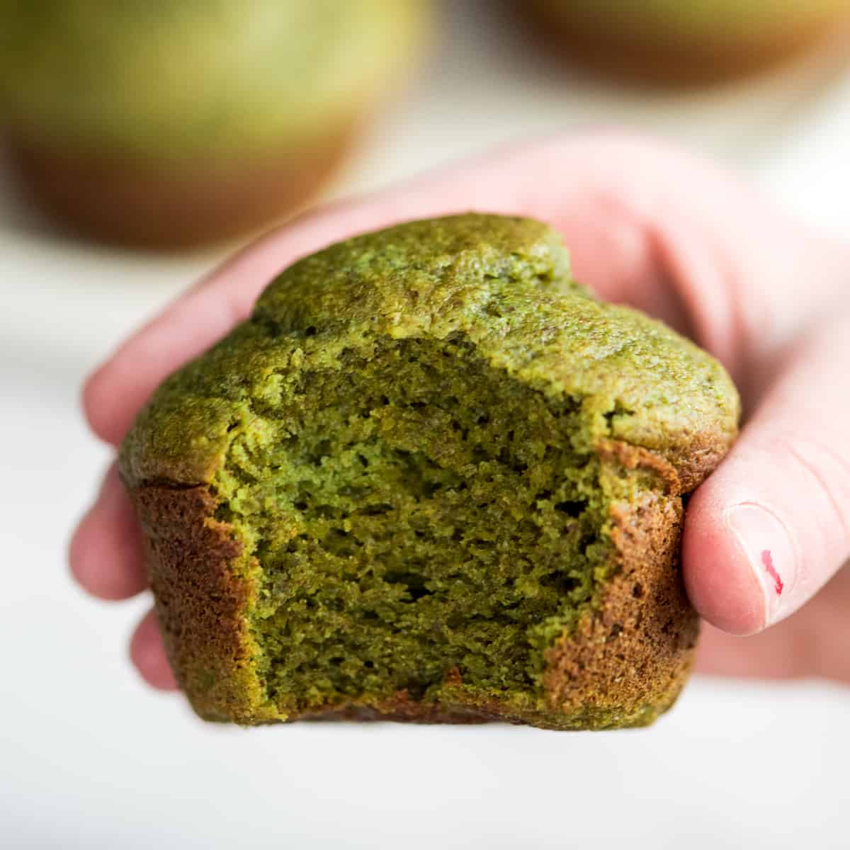 a hand holding a Banana Spinach Muffin with a bite taken out of it 
