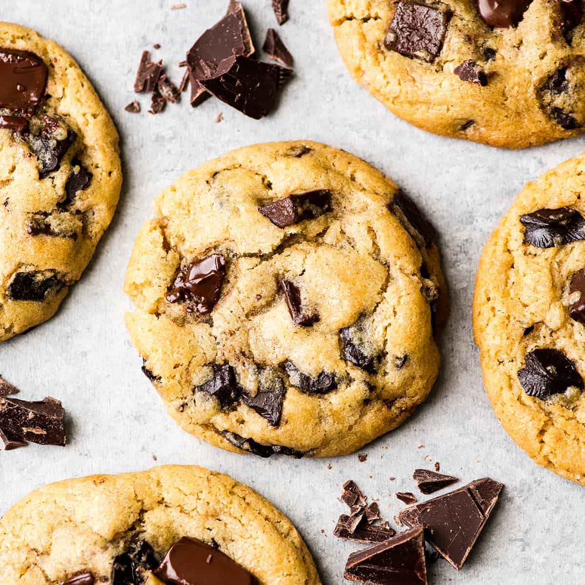 Overhead view of one chocolate chip cookie surrounded by four other chocolate chip cookies and chopped chocolate
