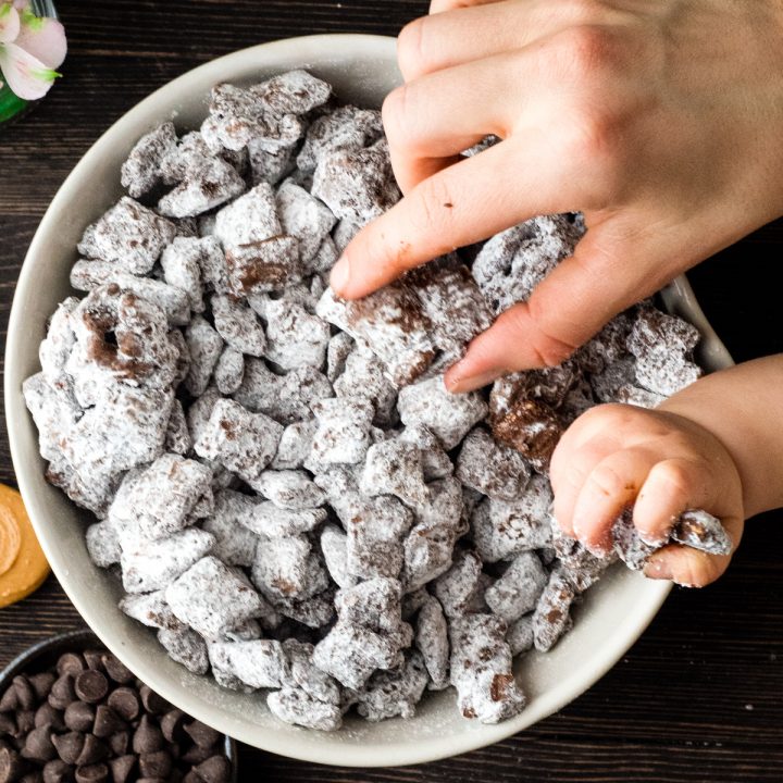 Overhead view of a bowl of the best puppy chow recipe in a bowl with two hands taking some out