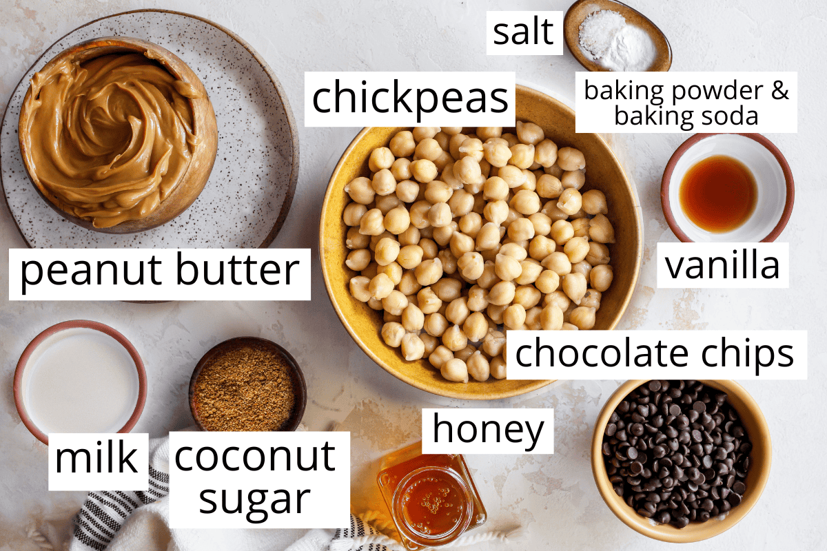 overhead photo of the labeled ingredients in this chickpea blondies recipe like chickpeas, peanut butter, coconut sugar and chocolate chips. All in bowls.