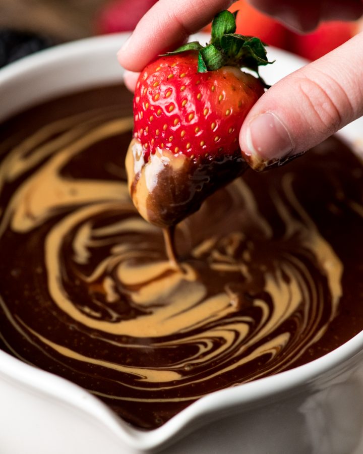 a strawberry being dipped into chocolate peanut butter fondue