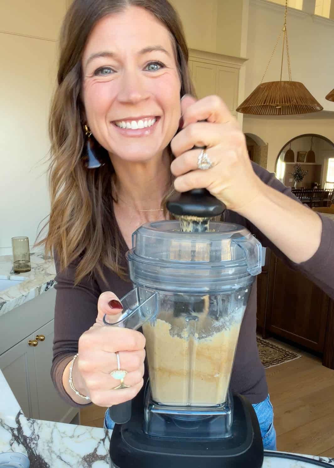 a woman smiling and blending the batter for these chickpea blondies in a vitamix blender.