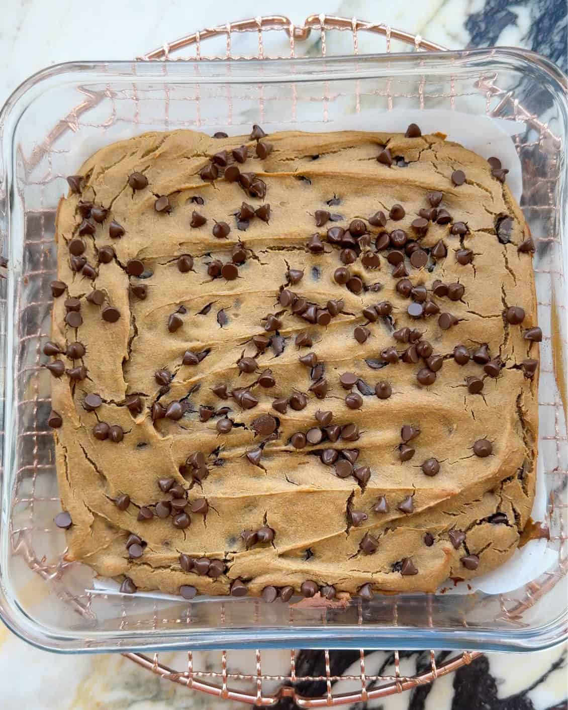 baked chickpea blondies in a square glass baking dish on a round copper wire cooling rack